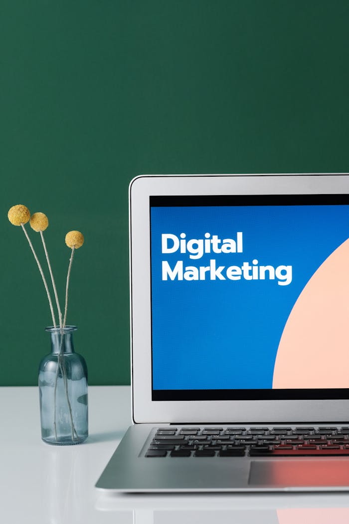 who-we-are A laptop displaying 'Digital Marketing' with a minimalist floral decor in a glass vase.