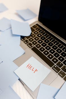 A laptop covered with sticky notes and a prominent "Help" sign, conveying urgency.